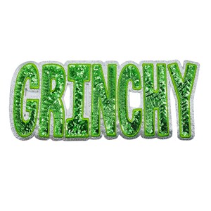 May include: A sequined, green "GRINCHY" word design with a silver glitter border. The letters are filled with green sequins, creating a sparkling effect. The design is likely a decorative item or accessory.