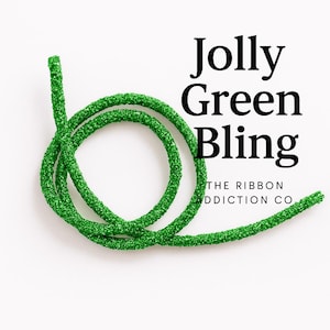 May include: A coiled length of sparkly, bright green ribbon. The text "Jolly Green Bling" is displayed in large, bold, black letters. The words "THE RIBBON ADDICTION CO" are displayed in smaller black letters.