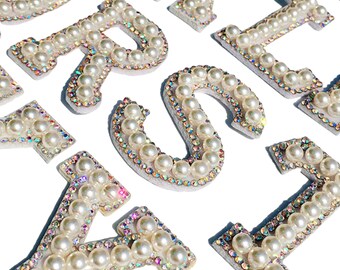May include: A set of pearl and rhinestone alphabet letters. The letters are white with iridescent rhinestones and white pearls. The letters are arranged in a random order. The letters are on a white background. The word "ENLARGED" is printed in black at the bottom of the image.