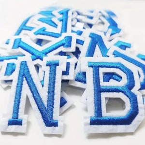 May include: A pile of blue felt letter patches with white outlines. The letters are N and B.