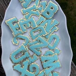 May include: A pile of turquoise blue felt letters with gold glitter trim. The letters are in various sizes and shapes.