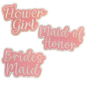 May include: Three pink fabric patches with white embroidered text. The patches read "Flower Girl", "Maid of Honor", and "Bridesmaid".
