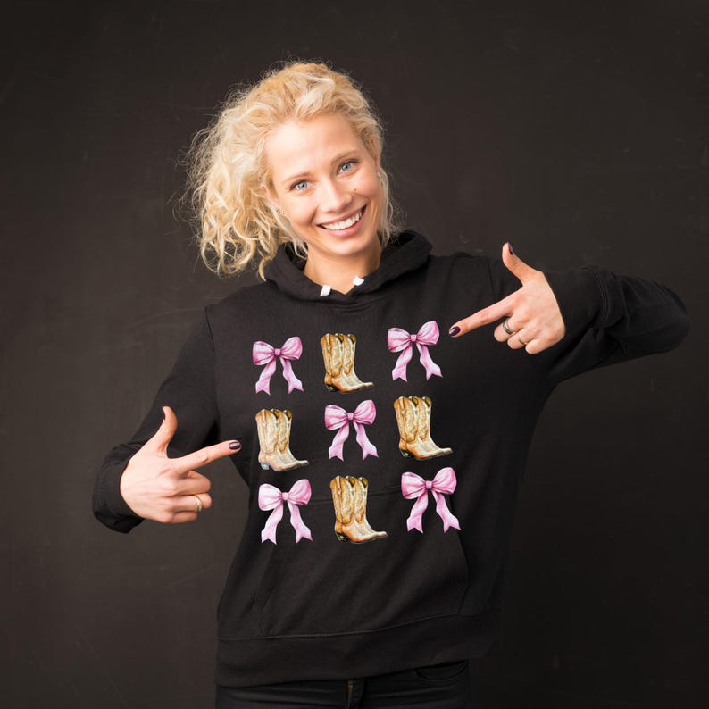May include: Black hoodie featuring a repeating pattern of cowboy boots and pink bows. The boots are tan with intricate detailing, and the bows are a soft pink. The design is centered on the front of the hoodie.