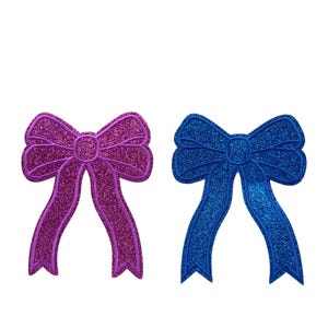May include: Two glitter bows, one purple and one blue. The bows are tied in a simple knot and have a shiny, sparkly finish.