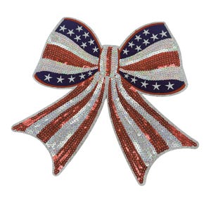 May include: A large, decorative bow featuring a patriotic design. The bow is adorned with red and silver sequins stripes, and blue sections with white stars. The bow is likely intended for festive occasions or patriotic displays.