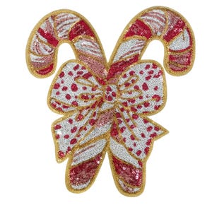 May include: A festive Christmas decoration featuring two candy canes and a bow. The candy canes are red and white with gold trim, and the bow is white with red polka dots. The decoration is covered in sequins.