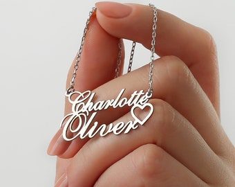 May include: Silver necklace with the names "Charlotte" and "Oliver" in cursive script, separated by a small heart charm.