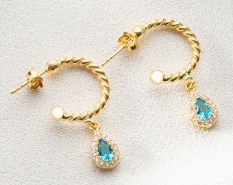 May include: A pair of gold hoop earrings with a teardrop-shaped blue gemstone pendant. The earrings are twisted and have a delicate design.