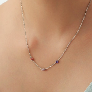 May include: A silver chain necklace with three small gemstones: red, pink, and purple.