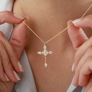 Puede incluir: Un collar de cadena dorada con un delicado colgante de cruz adornado con piedras transparentes brillantes.