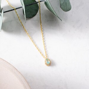 May include: A delicate gold chain necklace with a teardrop-shaped pendant featuring a light blue gemstone surrounded by smaller clear stones.