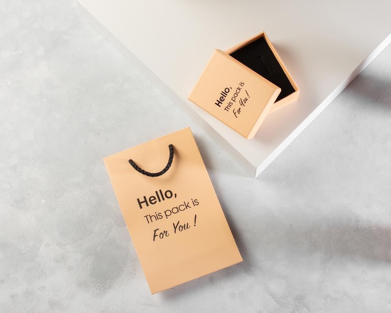May include: A light brown gift bag with black handles and the text "Hello, This pack is For You!" printed on it. A smaller light brown box with the same text is also shown.