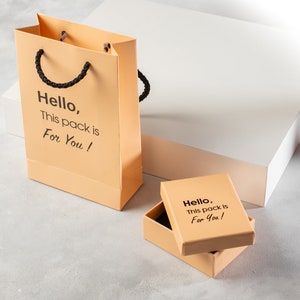 Puede incluir: Dos cajas de regalo naranjas con texto negro que dice "Hello, This pack is For You!" La caja m&aacute;s grande es una bolsa de compras con asas de cuerda negra.