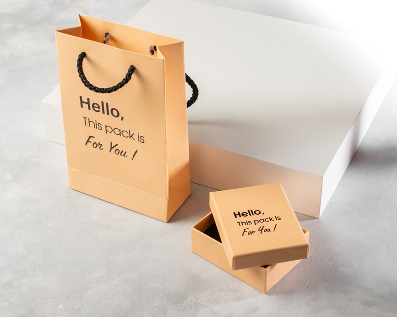Puede incluir: Dos cajas de regalo naranjas con texto negro que dice "Hello, This pack is For You!" La caja m&aacute;s grande es una bolsa de compras con asas de cuerda negra.