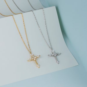 Puede incluir: Dos delicados collares con colgantes de cruz adornados con brillantes piedras de circonita c&uacute;bica transparentes. Un collar es dorado y el otro es plateado.