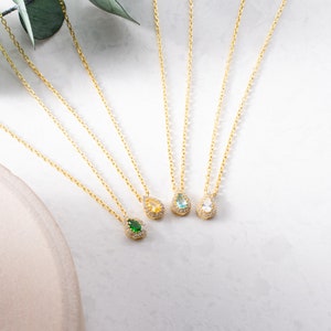May include: Four gold necklaces with teardrop-shaped pendants. Each pendant is set with a different coloured gemstone: green, blue, light blue, and clear.