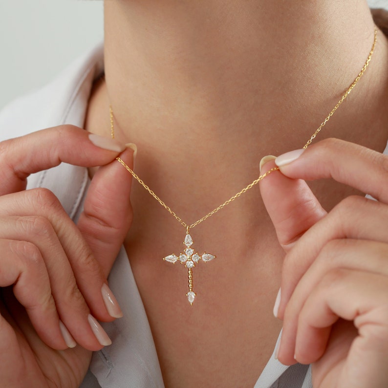 Puede incluir: Un collar de cadena dorada con un delicado colgante de cruz adornado con piedras transparentes brillantes.