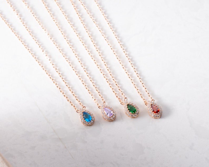 May include: Five gold necklaces with teardrop-shaped pendants. Each pendant is set with a different coloured gemstone: blue, purple, green, and red.
