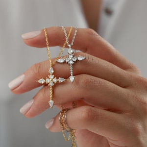 Puede incluir: Dos collares de plata y oro con un colgante de cruz de cristal. La cruz est&aacute; adornada con cristales transparentes en forma de pera.