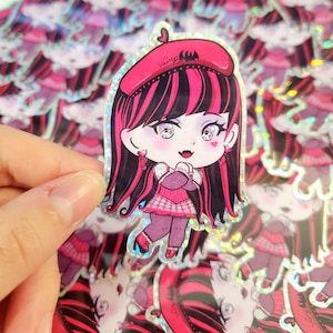 Puede incluir: Una pegatina holográfica con una niña de dibujos animados con cabello rosa y negro que lleva una boina rosa con la palabra "Vamp" en ella. Lleva una falda de cuadros rosa y negro y una camisa rosa con cuello blanco. Tiene las manos juntas frente a su pecho.