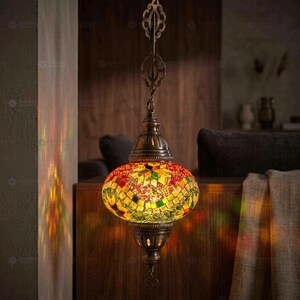 May include: A hanging pendant lamp featuring a spherical shade constructed from small, multi-coloured glass mosaic tiles in shades of red, yellow, and green. The lamp has an antique brass-toned metal fixture with a decorative chain and top loop.