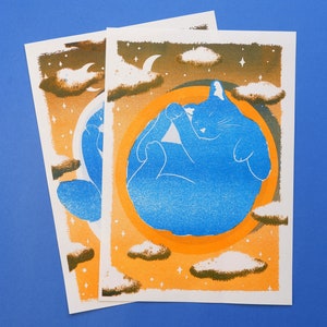 Peut inclure: Un chat bleu dort dans un cercle orange et jaune, entouré de nuages blancs et d'étoiles sur un fond brun.