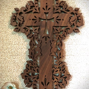 May include: A dark brown wooden cross with intricate floral carvings. The cross is made of walnut wood and has a distressed finish.