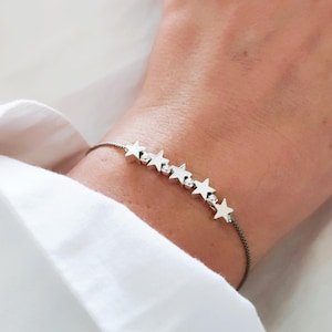 May include: A silver star charm bracelet with a black cord. The bracelet has seven silver stars.