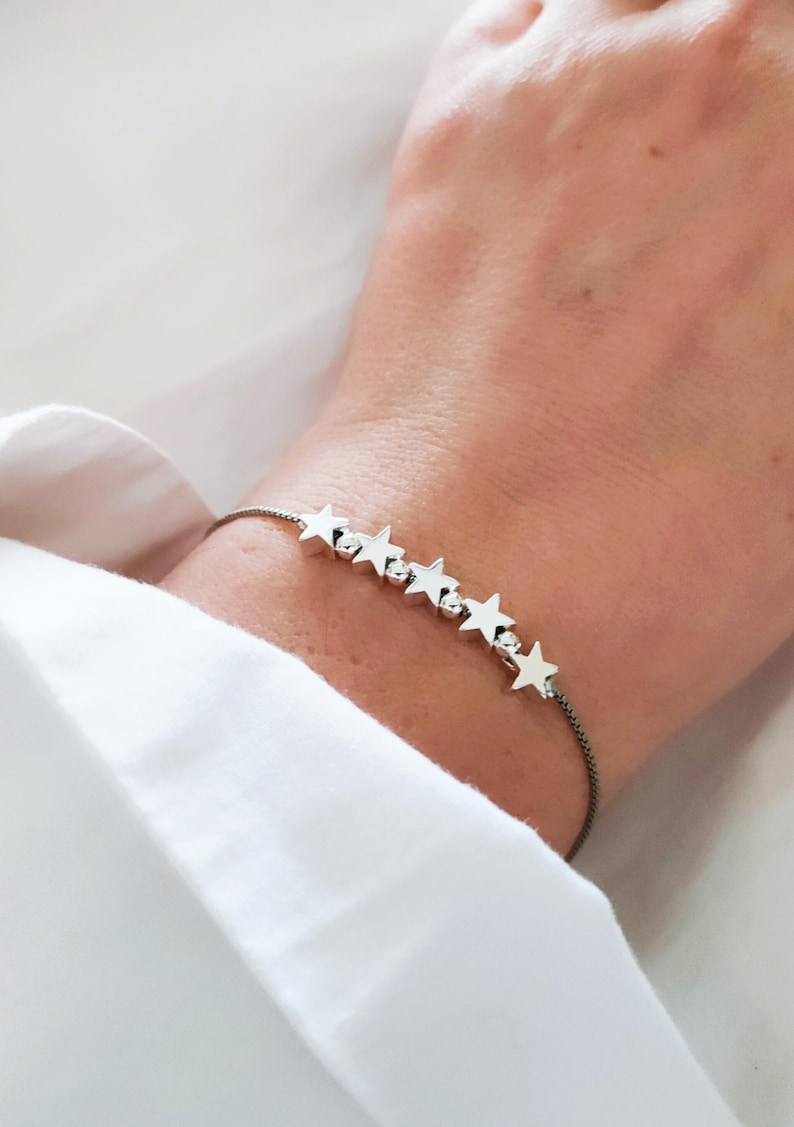May include: A silver star charm bracelet with a black cord. The bracelet has seven silver stars.