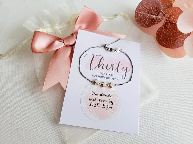 May include: A silver chain bracelet with three star charms. The bracelet is displayed on a white card with the text "Thirty Three Stars for Three Decades" and "Handmade with love by Lid'H Bijou".