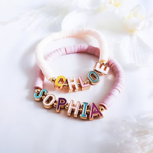 May include: Two bracelets with the names "Chloe" and "Sophia" spelled out in colourful letters. The bracelets are made of pink and white beads.