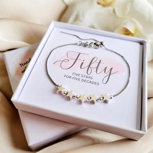 May include: A silver bracelet with five star charms in a white box. The box has the text "Fifty Five Stars for Five Decades" printed on it.