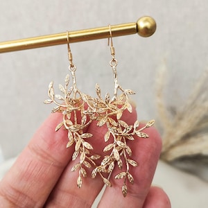 May include: Gold tone dangle earrings with a delicate leaf design. The earrings are long and feature multiple layers of leaves.