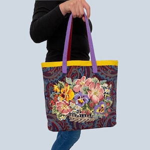 May include: A purple and yellow tote bag with a floral design. The bag features a basket of colorful flowers, including pink, yellow, and purple.