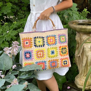 May include: A white crocheted tote bag with a colourful granny square pattern. The bag has bamboo handles and a pink lining.