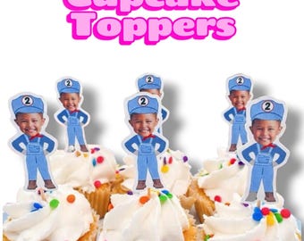 May include: Cupcake toppers featuring a cartoon illustration of a child wearing a blue train conductor outfit with a number 2 on the hat. The toppers are inserted into cupcakes with white frosting and colorful sprinkles. The text Cupcake Toppers is visible.