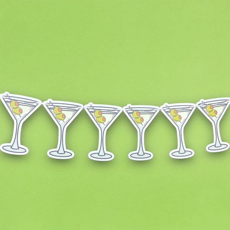 May include: A string of six white paper martini glasses with green olives, perfect for a party or celebration.