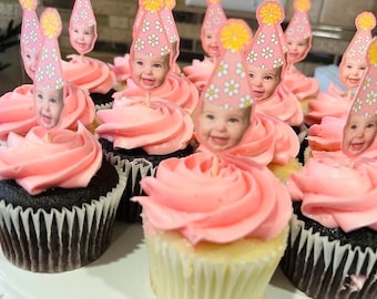 May include: A collection of cupcakes with pink frosting and baby-themed toppers. The cupcakes have a chocolate base and are topped with swirls of pink frosting. Each cupcake is decorated with a small image of a baby wearing a party hat.