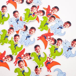 May include: A collection of colorful dinosaur stickers featuring a child's face. The stickers depict various dinosaurs in green, blue, and orange, with the child's face superimposed on each dinosaur. The child is wearing a yellow shirt and blue pants.