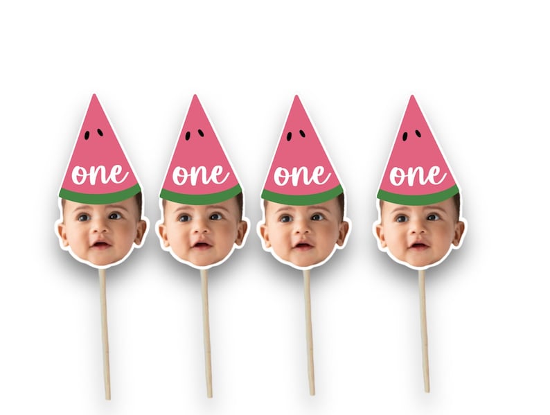 May include: Four watermelon-themed party decorations. Each features a baby's face with a pink watermelon slice hat, green rind, and the word "one" in white. The decorations are attached to wooden sticks.
