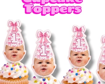 May include: Cupcake toppers featuring a baby's face wearing a pink party hat with a white bow and the number 1. The toppers are placed on cupcakes with white frosting and colorful sprinkles. The text Cupcake Toppers is at the top.