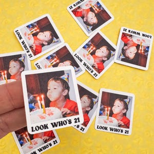 Puede incluir: Una colección de pegatinas cuadradas con una foto de una persona soplando las velas de una tarta de cumpleaños. Las pegatinas tienen el texto "LOOK WHO'S 21" impreso. El fondo es amarillo.