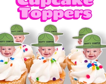 Op de afbeelding: Cupcake toppers met een lachend babygezichtje dat een groene rangerhoed draagt met de tekst Happy Camper op de rand gedrukt. De toppers zijn in cupcakes met witte glazuur en kleurrijke hagelslag gestoken. De tekst Cupcake Toppers staat bovenaan.