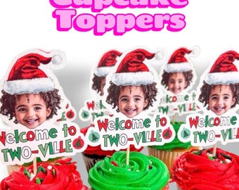 Op de afbeelding: Een set cupcake-toppers met een fotouitsnede van een kind met een rood-witte kerstmuts. Onder het gezicht staat een wit bordje met de rood-groene tekst Welcome to TWO-VILLE, versierd met kleine rode en groene kerstornamenten.