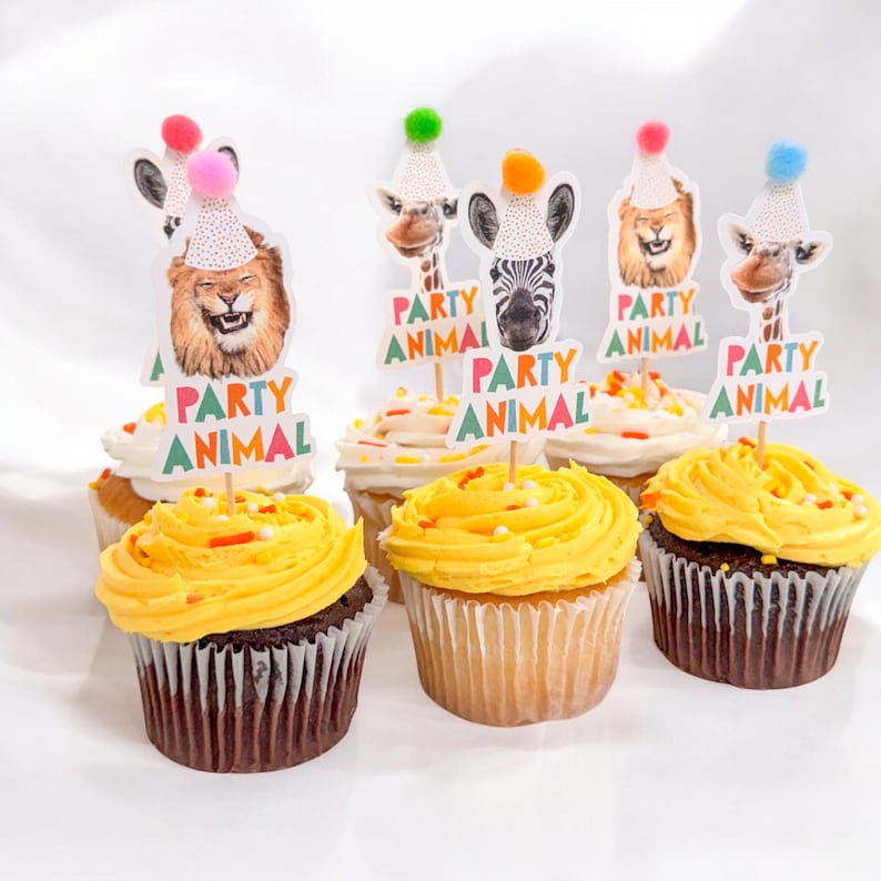Puede incluir: Seis cupcakes decorados con glaseado amarillo y chispas de colores. Cada cupcake tiene una decoraci&oacute;n tem&aacute;tica de animales de fiesta con un le&oacute;n, una cebra, una jirafa y un sombrero de fiesta colorido. Las decoraciones tienen el texto "Party Animal".