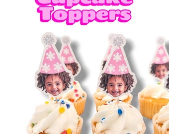 May include: A collection of cupcake toppers featuring a photograph of a child wearing a pink party hat with white snowflake patterns. The text Cupcake Toppers is displayed in large, bold, pink letters above the decorated cupcakes.
