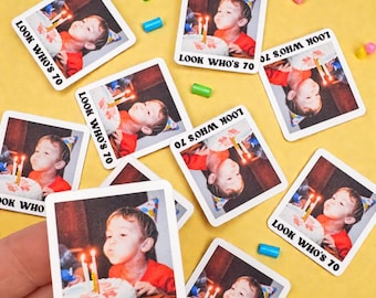 May include: A collection of square stickers featuring a child blowing out candles on a birthday cake. The stickers have the text "LOOK WHO'S 70" printed on them. The background is yellow with scattered colorful confetti.