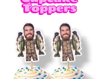 May include: Two cupcake toppers featuring a cartoon-style illustration of a bearded person in camouflage clothing holding a large fish in each hand. The text Cupcake Toppers is displayed in large pink letters above the two decorated cupcakes.