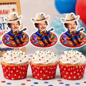 Op de afbeelding: Drie cupcakes in rood-witte stippenpapiertjes met witte glazuur en gekleurde spikkels. Elke cupcake heeft een papieren topper met een afbeelding van een kind met een cowboyhoed dat gitaar speelt terwijl het op een rode zwemband zit.