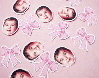 May include: A collection of stickers featuring a baby's face and pink bows on a pink background. The baby stickers show a smiling infant with brown hair. The pink bows have a white outline. The stickers are scattered across the pink surface.